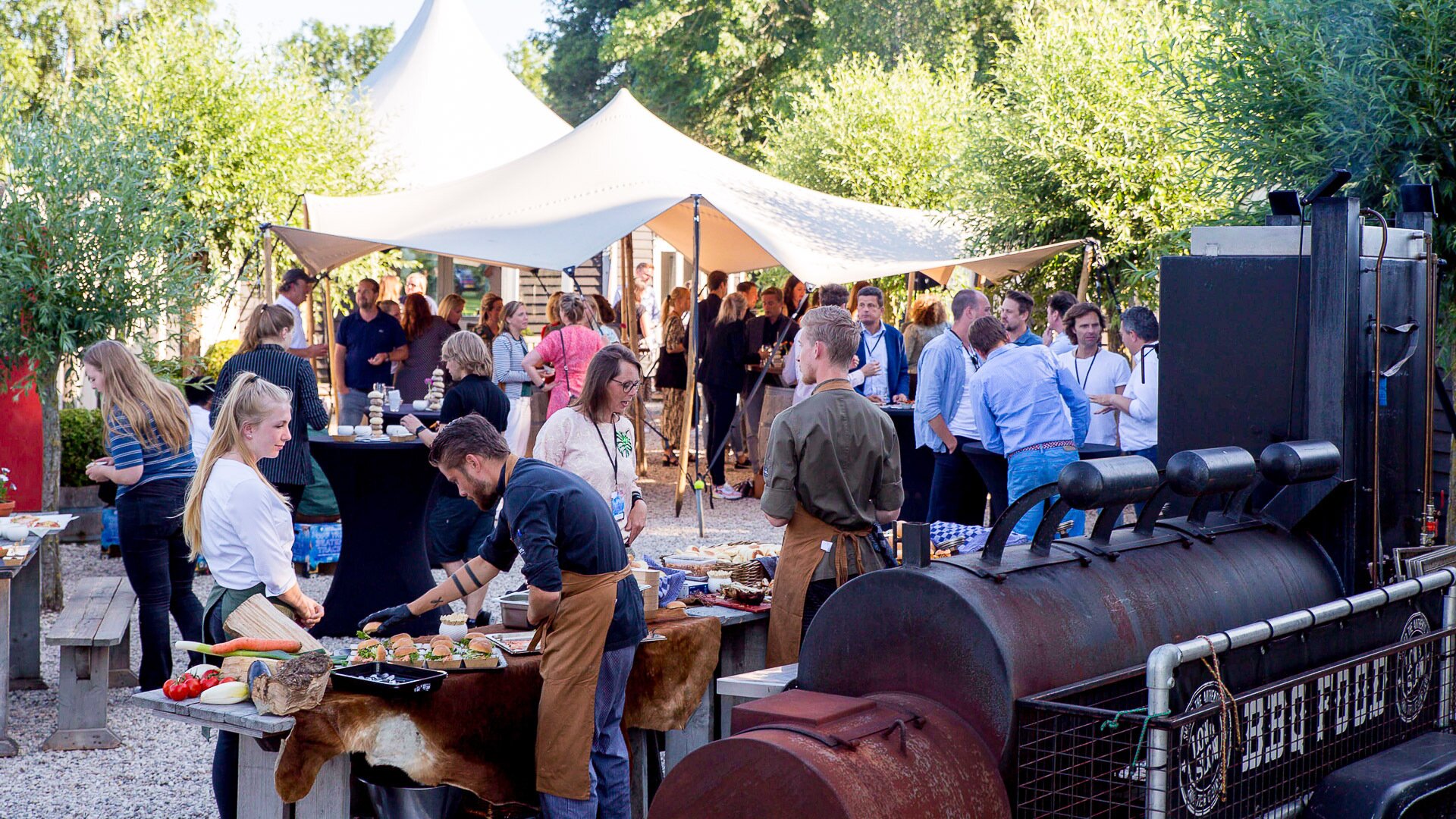 uitzicht op een borrel bij de veldhuisjes met een pagode tent, buffet met hapjes en veel kletsend publiek.